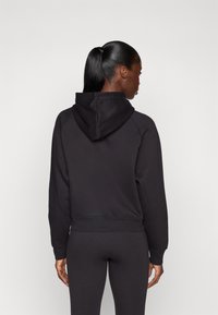 Svart hettegenser med en kort design, teksturert stoff og ribbestrikkede ermer, kombinert med matchende svarte leggings.