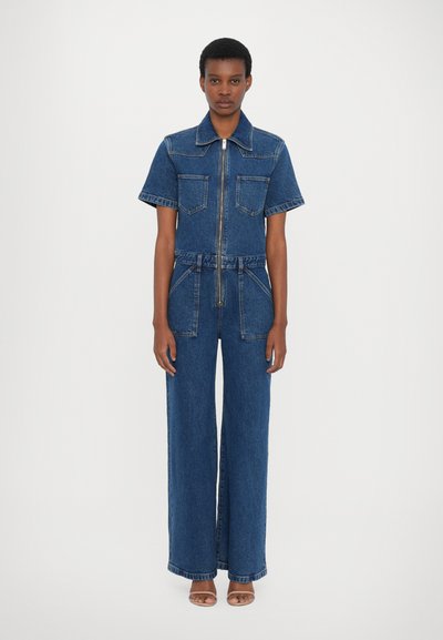 Denim jumpsuit i mørkeblå. Korte ærmer, krave, frontlynlås, to brystlommer og bred benvidde. Glat tekstur og robust materiale.