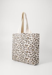 Tote bag s leopardím potiskem vyrobený z plátna s béžovými a hnědými vzory. Disponuje pevnými béžovými ušima. Obdélníkový tvar se plochým dnem.
