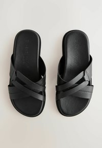 Sorte slidesandaler med flere krydsseler og en glat finish. Sålen er flad med en rund tådesign, lavet af kunstlæder.