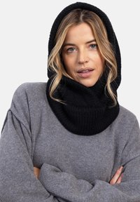 Czarny sweter z kapturem o fasonie z kołnierzem, z teksturowym wykończeniem. Noszony na jasnoszarym swetrze z luźnymi rękawami.