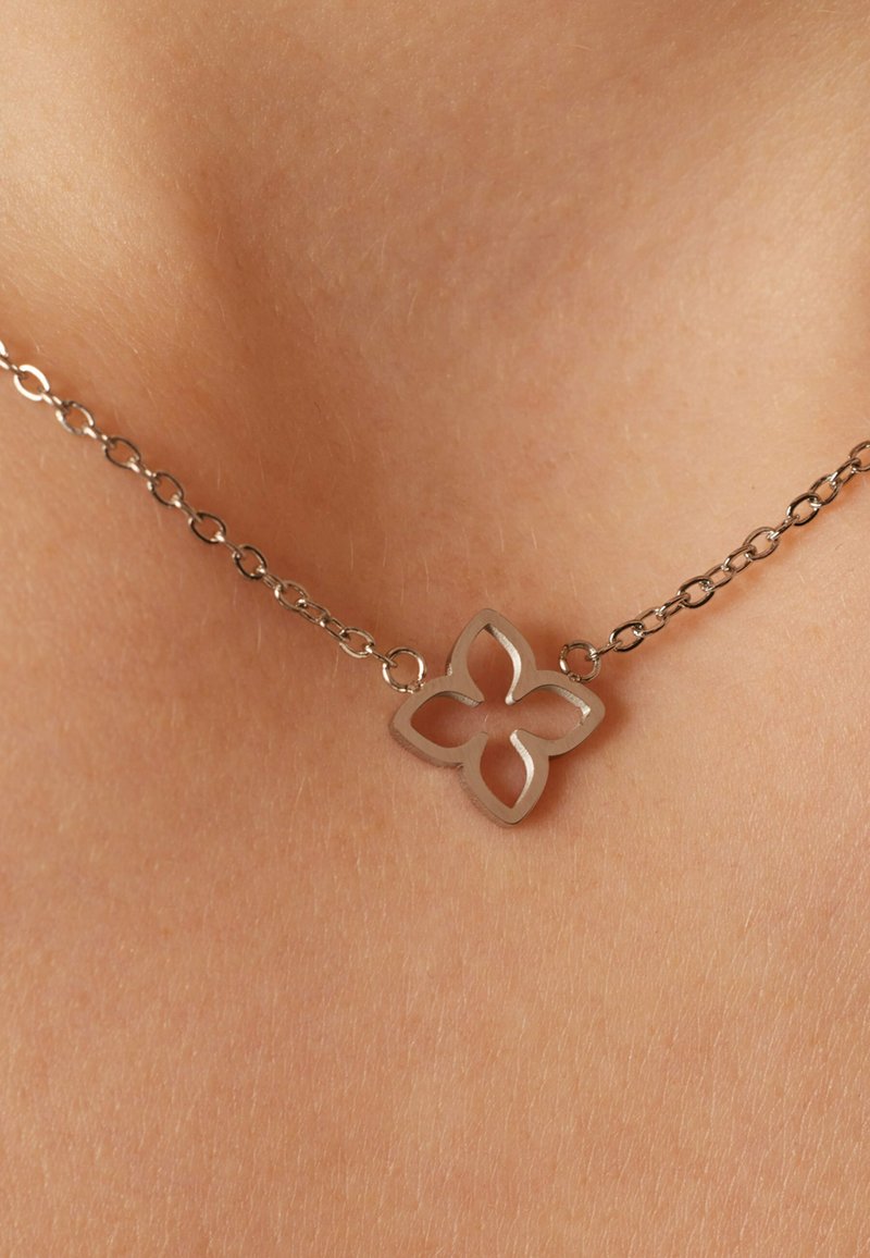 Zilveren ketting met een uitgesneden bloemenhanger met een gladde afwerking, rustend op een lichte huidtint.