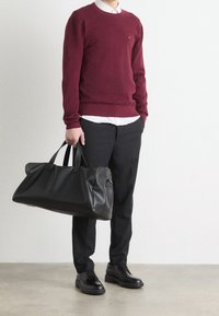 Sac de voyage en cuir noir à la forme structurée, texture lisse et poignées doubles. Pull bordeaux chaud porté sur une chemise blanche à col.