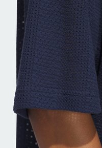 Marinblått stickat tyg med en texturerad, öppen väv. Sömmen är avslutad med en slät kant, vilket kontrasterar med det mönstrade materialet.