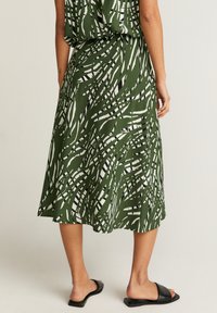 Grüne Rock mit einem fließenden Design, das weiße und schwarze abstrakte Muster aufweist. Hergestellt aus leichtem Material, hat er eine lockere Passform und eine mittellange Länge.