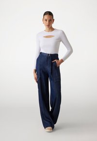 White long-sleeve top with a cut-out at the chest, paired with dark blue wide-leg cargo pants featuring two side pockets and a belted waist.