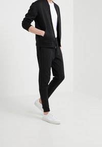 Svart idrottsjacka med dragkedja, ribbade ärmslut och sidofickor, kombinerad med svarta smala byxor och vita sneakers. Slät tygfinish.