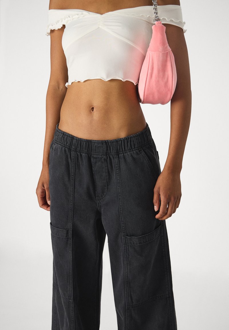 Biały top w stylu off-the-shoulder z falbankami, połączony z czarnymi, luźnymi spodniami cargo z kieszeniami oraz różową puszystą torebką.