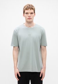 Light green cotton t-shirt with short sleeves, crew neckline, and subtle brand logo. Smooth texture and relaxed fit.