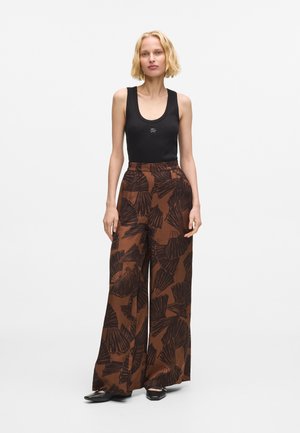 Czarny top na ramiączkach z okrągłym dekoltem, zestawiony z brązowymi spodniami o wysokim stanie i szerokich nogawkach, ozdobionymi czarnym wzorem liści. Czarne mokasyny.