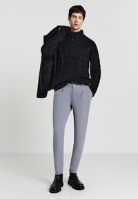 Maglione a collo alto nero lavorato a trecce, pantaloni grigi su misura e stivaletti neri alla caviglia. Il maglione presenta un design testurizzato; i pantaloni hanno una vestibilità slim.