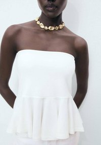 White strapless peplum top made of soft fabric, featuring a flared hem. Paired with a chunky gold necklace. Smooth texture and simple design.