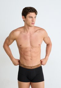 Boxers en coton noir avec une ceinture élastique marron arborant le logo "TOMMY HILFIGER". Le modèle ajuste la ceinture.