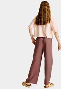 Lichtroze cropped t-shirt, losse pasvorm, gecombineerd met vloeiende, roestkleurige wijde broek. Getextureerde stof; bruine sandalen met decoratieve accenten.