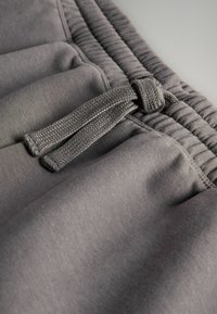 Pantaloni sportivi grigi con elastico in vita e cordino, texture in tessuto morbido e dettagli arricciati lungo la vita.