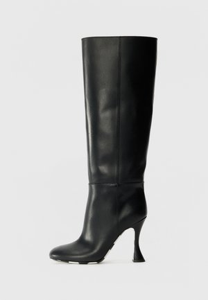 Botte en cuir noir, montante jusqu'au genou, avec un tige ajustée et un bout pointu. Présente un talon courbé distinctif et une surface lisse et texturée.