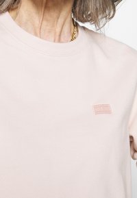 T-shirt a girocollo di colore rosa chiaro, realizzato in cotone, con un piccolo logo ricamato sul petto. Tessuto morbido e maniche corte.
