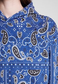 Felpa blu con motivo paisley in bianco e nero, realizzata in tessuto testurizzato e dotata di cappuccio con cordino. Decorata con cuori e motivi floreali.
