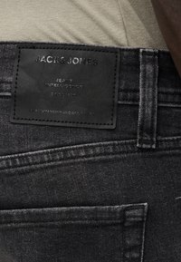 Μαύρα τζιν από τζιν ύφασμα με υφασμένη μαύρη δερμάτινη ετικέτα που εμφανίζει τις λέξεις «JACK & JONES», «JEANS INTELLIGENCE» και «SINCE 1990» σε ανάγλυφη γραφή.