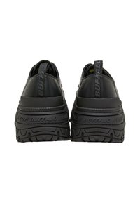 Coppia di scarpe platform nere con suole spesse e battistrada pronunciato, marchiate "BUFFALO" sulle linguette del tallone e sulle fasce della suola intermedia, viste da dietro.