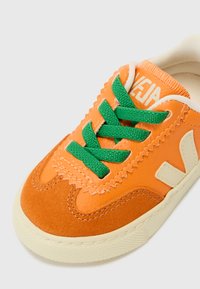 Sneaker con tomaia in camoscio e pelle arancione, lacci verdi, rifiniture avorio e suola in gomma testurizzata. Presenta un design a cofano e un marchio.