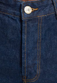 Denim jeans with a dark blue color, featuring gold stitching and a round metal button labeled "DEF" at the waistband.