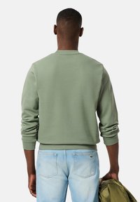 Sudadera verde de algodón con cuello redondo y mangas largas, que presenta puños y dobladillo acanalados, combinada con vaqueros de mezclilla azul claro.