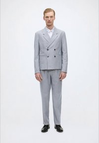 Ανοιχτό γκρι διπλό ραμμένο κοστούμι με δομημένο σακάκι και ίσια παντελόνια. Λείο ύφασμα, ελάχιστες λεπτομέρειες, σε συνδυασμό με μαύρα παπούτσια.