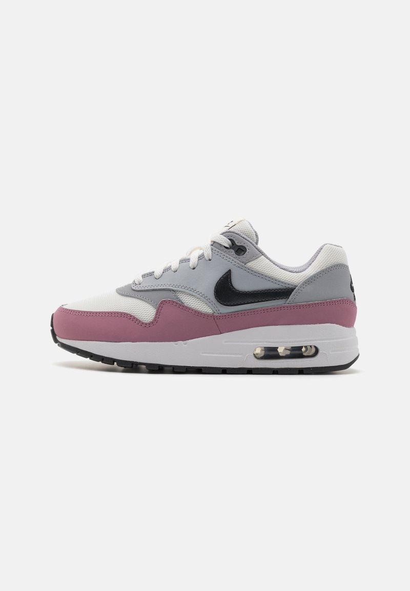 Nike Air Max 1 jalatsid on valge ja halli võrgumaterjaliga ülemine osa, roosa vahepealne osa, mustad aktsendid ja nähtav õhkuunit tagakannikul.