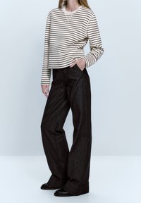 Top a maniche lunghe a righe in crema e marrone, abbinato a pantaloni a gamba larga neri a vita alta. Presenta una vestibilità rilassata e tasche laterali.