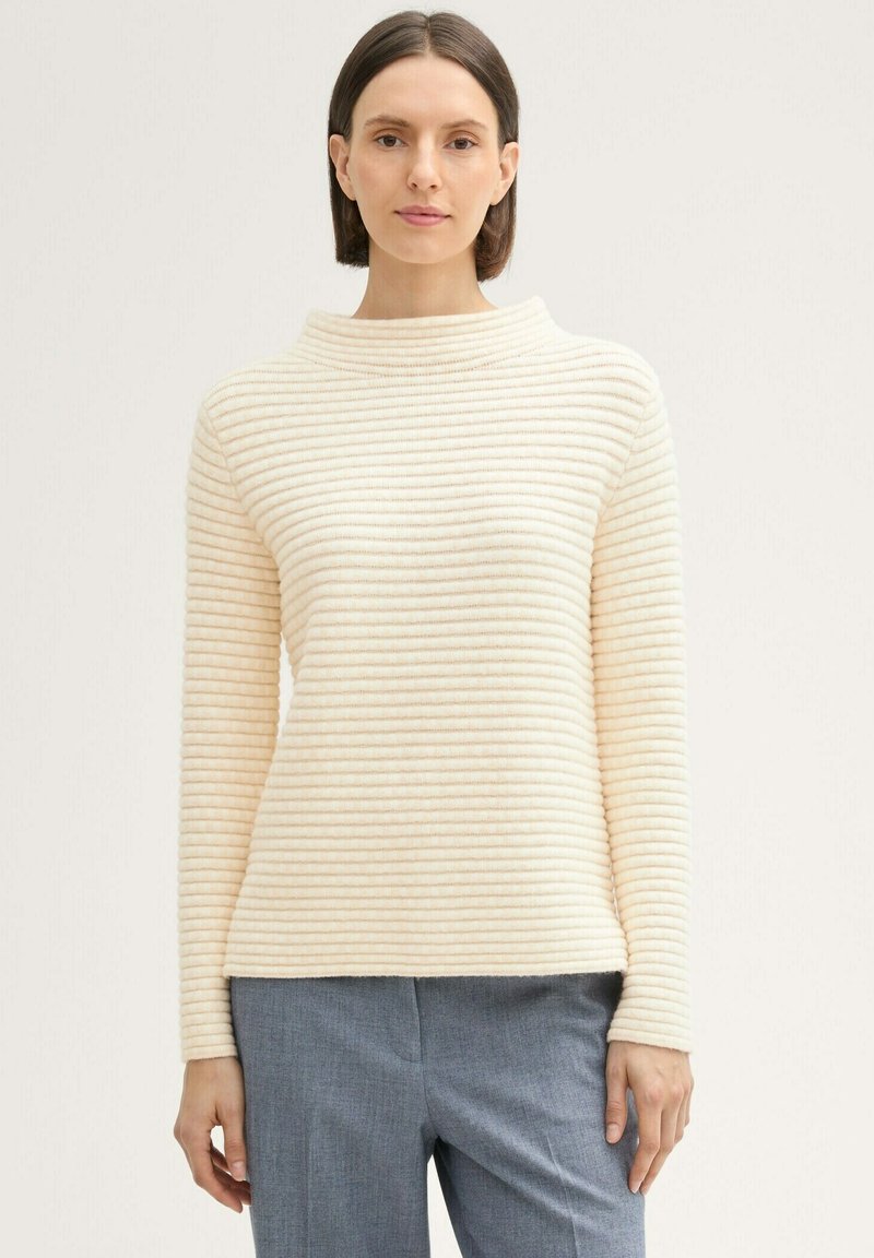 Pull en maille à rayures couleur crème avec un col haut et des manches longues, présentant des lignes texturées horizontales sur le tissu.