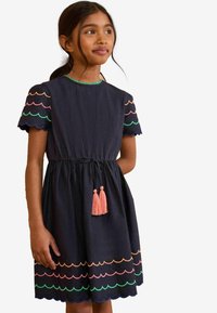 Rochie bleumarin cu mâneci scurte cu margini ondulate, având modele colorate de scoici și ciucuri roz la talie. Fabricată din material ușor.