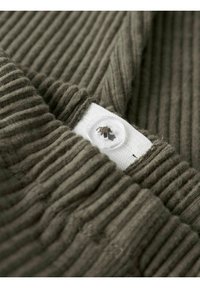 Tissu côtelé vert olive mettant en valeur une fermeture à bouton blanc avec des détails de couture visibles, soulignant la texture et la profondeur du matériau.