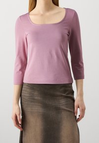 Vaalean violetit kolme neljännesosa hihat topit, joissa on neliön muotoinen kaula-aukko, valmistettu sileästä kankaasta. Vaatteen päällä on ruskea teksturoitu hame.