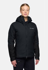 Zwarte geïsoleerde jas met capuchon, ritssluiting aan de voorkant en zijzakken. Heeft een zachte textuur en contrasterend materiaal op de mouwen. Vaude-logo zichtbaar.