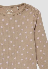 Beige geribd babyshirt met lange mouwen, lichtroze stippen en twee drukknoopjes op de schouder voor gemakkelijk aankleden.