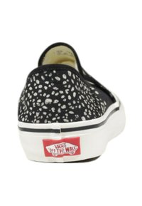 Scarpa slip-on nera in tela con motivo maculato bianco, suola bianca, striscia nera e logo rosso "VANS OFF THE WALL" sul tallone.