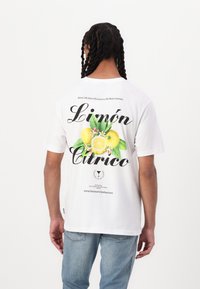 Valkoinen t-paita, jossa on sitruunagrafiikka vihreillä lehdillä, musta teksti "Limón" ja "Cítrico" sekä ylimmässä osassa kuvitusta oleva lisäteksti.