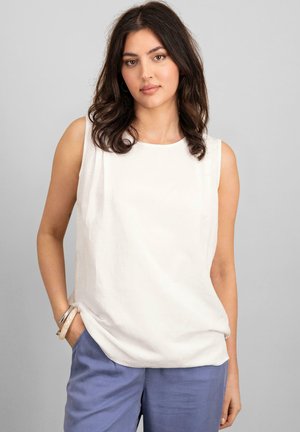 Camicia bianca senza maniche, realizzata in tessuto morbido, con scollatura rotonda e vestibilità comoda. Abbinata a pantaloni azzurri chiari.