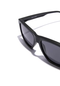 Ochelari de soare negri cu un design dreptunghiular și unghiular. Realizați din plastic mat. Lentile întunecate. Marcate "Fabricat în SPANIA" pe bratul interior.