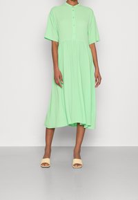 Vihreänmintun värinen, lyhythihainen mekko, jossa on napillinen kaulus, liehuva helma ja rento istuvuus. Yhdistetty beigeihin liukusandaaleihin.