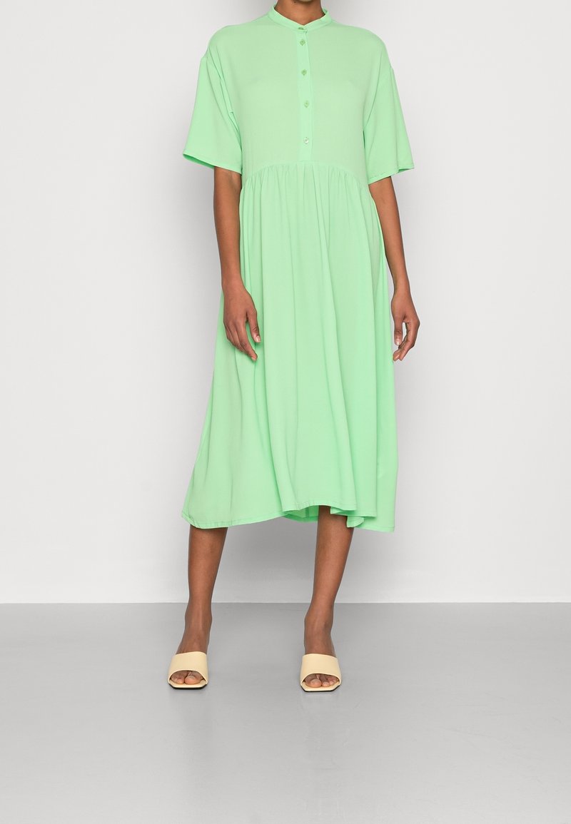 Vihreänmintun värinen, lyhythihainen mekko, jossa on napillinen kaulus, liehuva helma ja rento istuvuus. Yhdistetty beigeihin liukusandaaleihin.