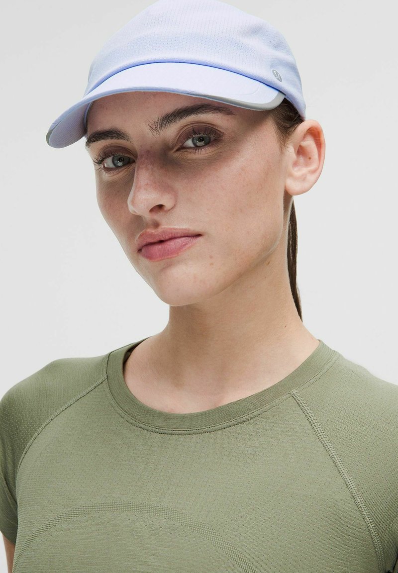 Gorra azul claro con visera curvada, hecha de tela texturada. Llevada con una camiseta verde oliva ajustada que presenta un escote redondo y patrones sutiles.