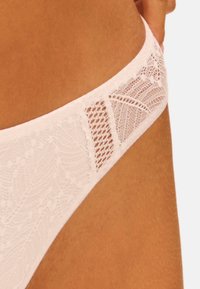 Witte kanten string met ingewikkelde bloemenpatronen, contrasterende gladde stof en een doorzichtige kanten strook bij de taille. Zachte en lichte textuur.
