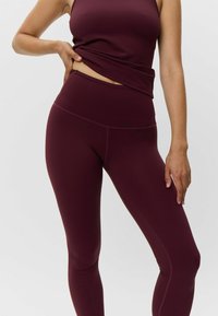 Bordo aktyvios aprangos komplektas, kuriame yra prigludusi liemenėlė ir aukšto liemens leggingai; lygi tekstūra su kontrastingomis siūlėmis.