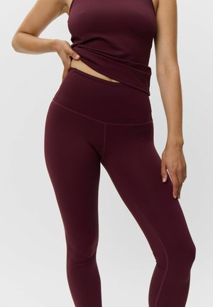 Burgundin väri aktiivivaatteet, johon kuuluu tiukasti istuva toppi ja korkeavyötäröiset legginsit; sileä pinta, jossa on kontrastiväriset ommelyksityiskohdat.