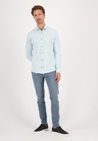 Svetlo modra srajca s dolgimi rokavi in gumbi, sivi slim-fit hlače in črne superge. Srajca ima klasičen ovratnik in sprednje gumbe.