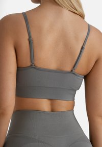 Top sportivo grigio con spalline sottili e texture a coste. Presenta un design aderente e una fascia elastica, mettendo in mostra una schiena senza cuciture.