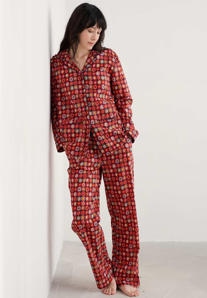 Punainen kuvioitu pyjama, jossa on napitettava yläosa ja löysät housut, joita koristavat värikkäät timanttipäät. Valmistettu pehmeästä kankaasta.