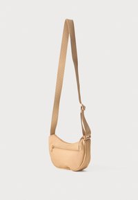 Brun crossbody-veske med en myk, buet form og en frontlomme med glidelås. Bred stoffrem for enkel bæring. Glatt tekstur.
